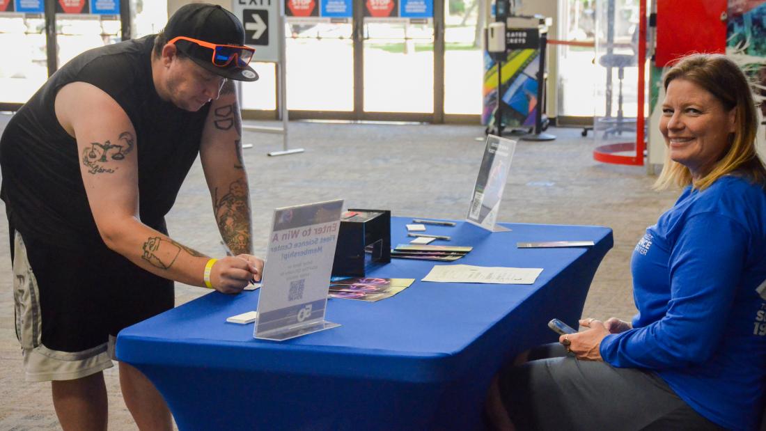 Fleet staff sitting behind a table with a blue tablecloth and guest standing while filling out and enter-to-win form