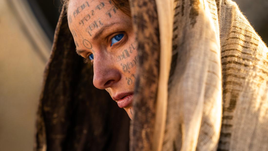 Production still from Dune part two close up of a woman in a hood with blue tattoos on her face