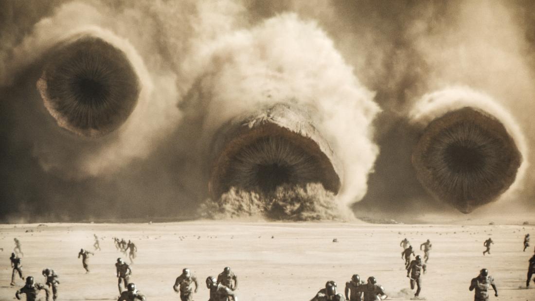 Production still from Dune part two of a massive dust storm with people running in the foreground