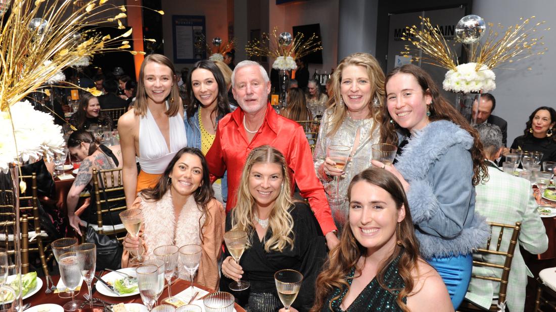 A group of people standing over one side of a rounded table smiling for the camera