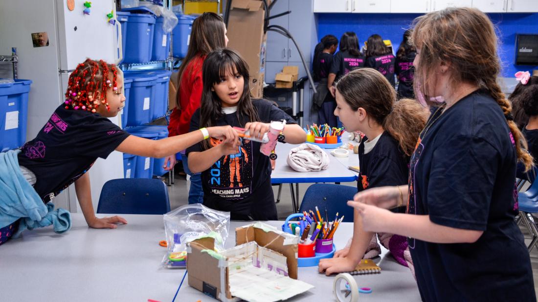 A group of 4 young girls around a work table working on a craft science project