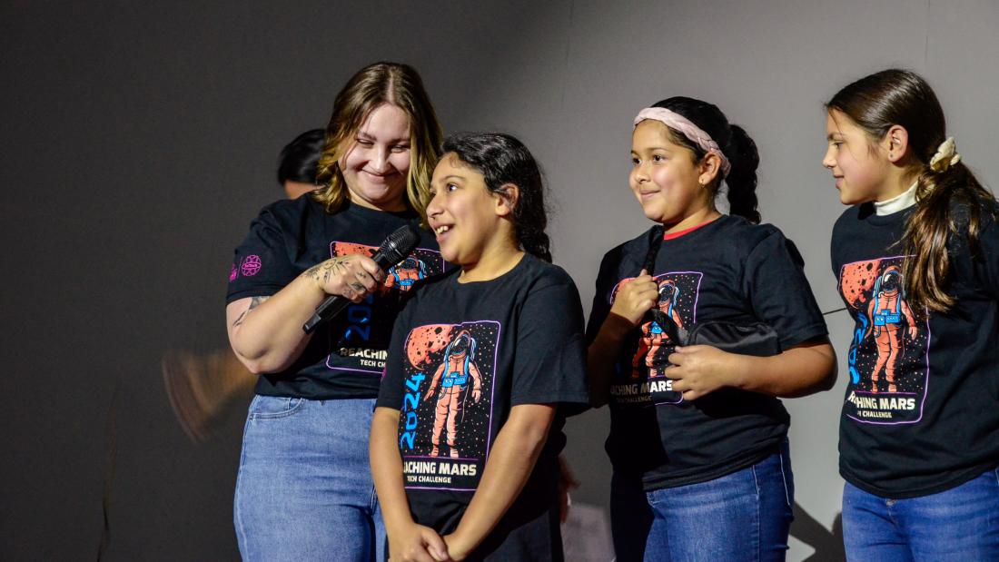 A woman holds a microphone next to a young girl and two other girls 