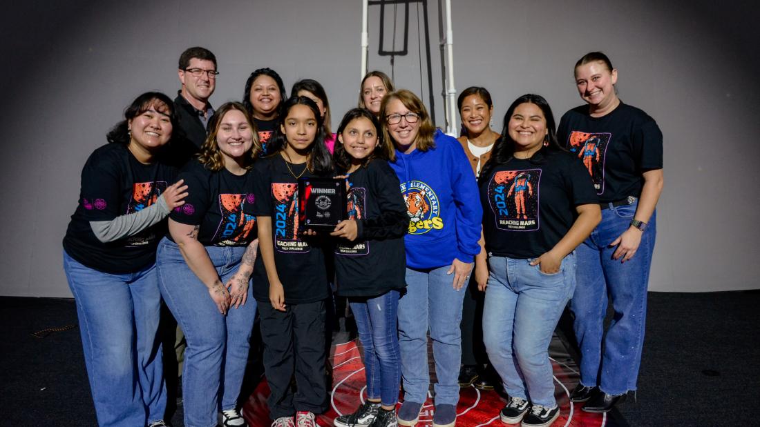 A group of women pose with two girls who hold and award and smile