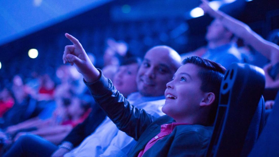 boy in crowd points at IMAX screen during movie