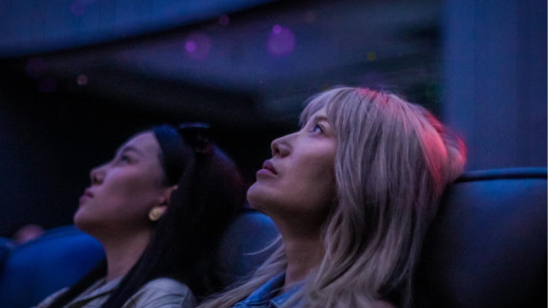 Two women in a theater watching towards the screen, mesmerized. 