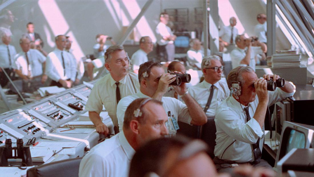 NASA managers Walter Kapryan (leaning on console), Rocco Petrone (with binoculars, center), and Kurt Debus (with binoculars, right) watch from Kennedy's Launch Control Center.
