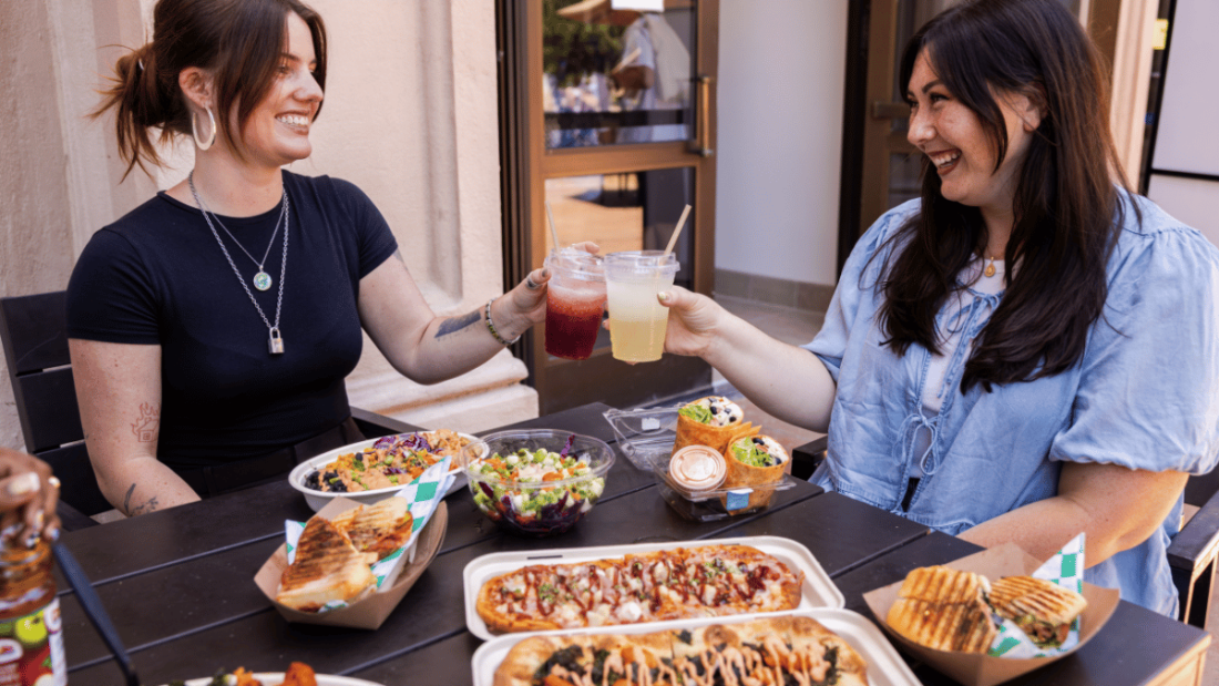 Guests cheersing drinks sitting at table with assortment of food