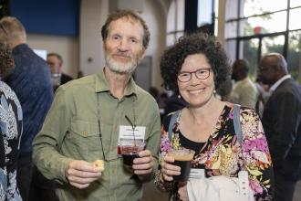 A man and woman holding cups of wine stand together and smile