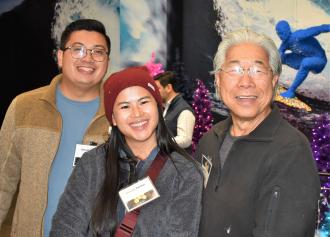 Two men either side a woman wearing a red beanie smile in a crowded room