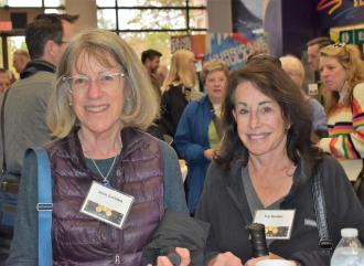 Two women wearing name tags smile in a very crowded room