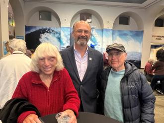 An older woman and two older men pose and smile together