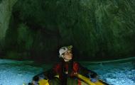 Scientist looking to their left inside of a large cave. The Sciectist is in a yellow raft atop blue water.