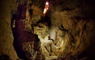 A cave diver lowering themselves into a large cave.