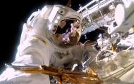 An astronaut wearing a full suit and helmet outside of the ISS taking a selfie.