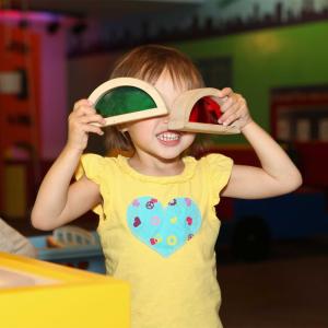 Toddler girl in a yellow shirt holding half circle shapes in front of her eyes with green and red see through panels