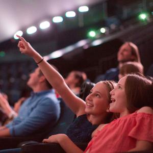 Two girls sitting in the imax theater with the girl on the left pointing to the screen