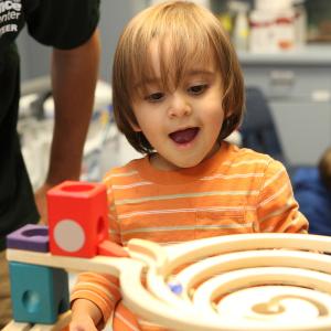 A toddler boy looks at a marble run and smiles widely
