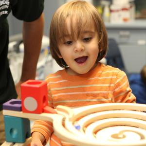 A toddler boy looks at a marble run and smiles widely