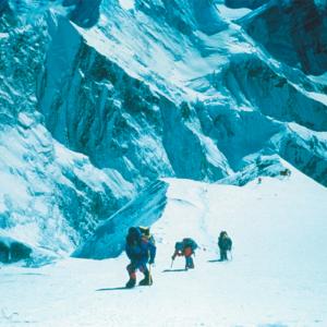 A blue filtered photo of three figures trekking up Mt. Everest.