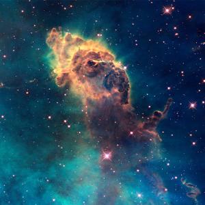 A Hubble image of deep blue and green space with many shining stars. The center is a brown-orange cloud of space dust in a puffy long shape.