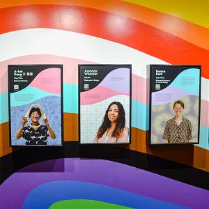 Three portrait panels in black frames sit on a wavy rainbow wall