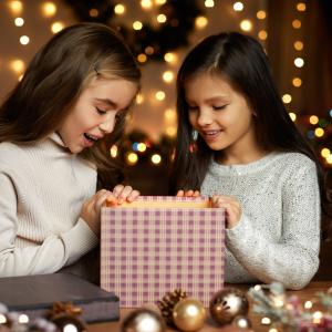 Two young girls open a gift during the holidays surrounded by lights 