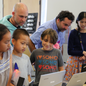 Children and adults surrounded around a computer.