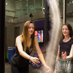 Two young adults moving their hands through the Tornado interactive at the Fleet Science Center