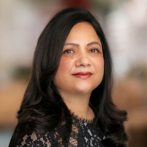 An indian woman at three-quarter profile with shoulder length dark hair and a black lace top. 