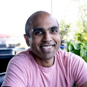 An indian man in a pink tshirt smiles at the camera 