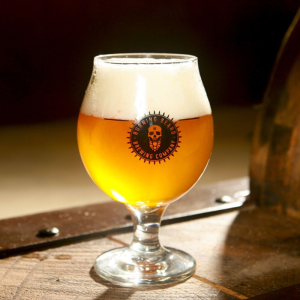 A glass with light beer next to a wooden barrel