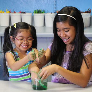 Two young girls squishing slime inside of a classroom.