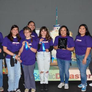 Group of young women and a female teacher in purple shirts pose at the SciTech Challenge competition