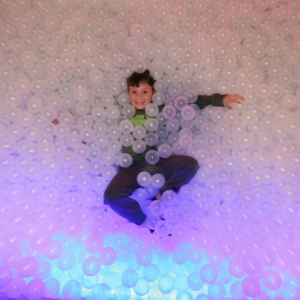 Kid in a ball bit surrounded by white translucent balls with a blue and purple ligth