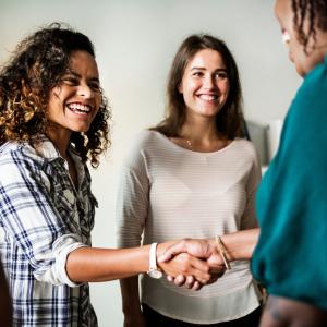 Two women smile and introduce themselves to a foreground woman who is out of frame