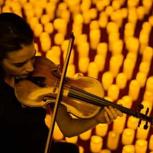 A woman playing violin surrounded by hundreds of candles
