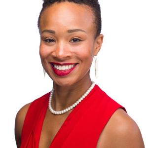 A black woman with short cropped hair in a red top with a white pearl necklace 