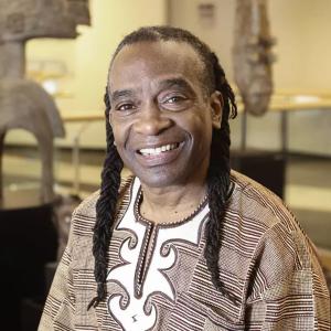 A black man in a brown top smiling in a museum artifact setting