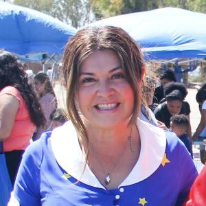 A woman in a blue and white top outside in a crowded area smiling