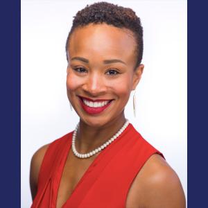 A black woman in a red top with a pearl necklace and red lipstick smiling  