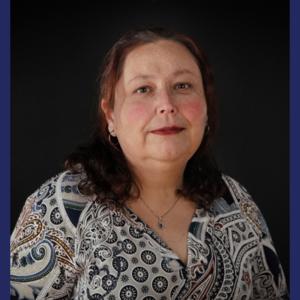 A hispanic woman in a patterned top against a dark background 