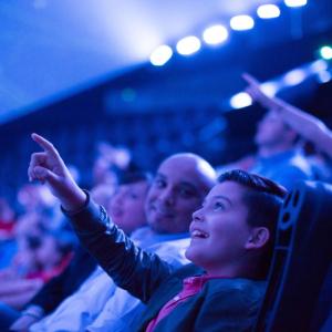 boy in crowd points at IMAX screen during movie
